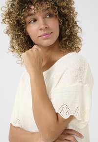 Maglione lavorato a maglia in bianco sporco con maniche corte, caratterizzato da una finitura testurizzata, motivi a punto aperto e dettagli con bordo a onde.