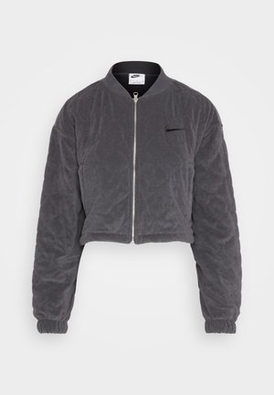 Beskaaret grå bomberjakke lavet af blødt, quiltet materiale. Har en frontlynlås, ribbet krave og elastiske manchetter. Nike-logo på brystet.