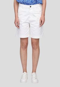 Shorts en coton blancs avec des revers, poches avant et fermeture à bouton, associés à des baskets blanches et un haut à fleurs bleues.