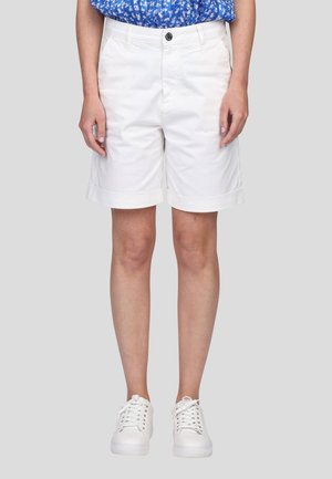 Shorts en coton blancs avec des revers, poches avant et fermeture à bouton, associés à des baskets blanches et un haut à fleurs bleues.