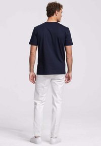 Marineblauwe katoenen t-shirt met korte mouwen, ronde hals en een ontspannen pasvorm, gedragen met witte broeken en witte sneakers.