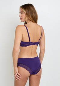 Set di lingerie viola con bordi in pizzo sul reggiseno e sulle mutandine, spalline regolabili e texture liscia. Vista posteriore in evidenza.