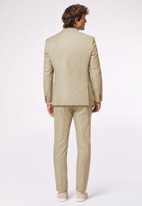 Helles beiges Anzug mit strukturiertem Finish, bestehend aus einer taillierten Jacke und einer maßgeschneiderten Hose. Das Design umfasst dezente Nähte und Knöpfe.