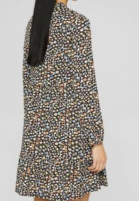 Robe noire à fleurs avec des manches longues, présentant un motif de petites fleurs jaunes, roses et bleues. ourlet volanté et texture de tissu léger.