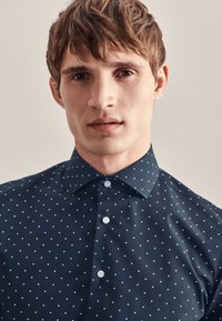 Marineblauw overhemd met knopen en een polkadotpatroon, voorzien van een klassieke kraag en witte knopen, met een gladde textuur en een aansluitend model.