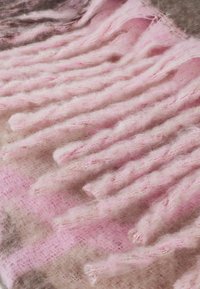 Écharpe tricotée rose clair et beige avec des détails de frange texturée. Matériel doux et duveteux présentant un motif dégradé et des brins délicats.