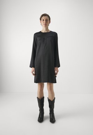 Abito nero a maniche lunghe con scollatura curva e texture liscia, abbinato a stivali da cowboy neri alti con punta affusolata.