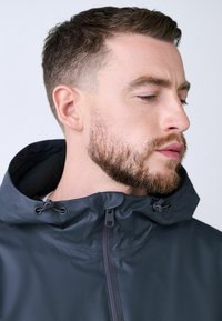 Tamnosiva vodootporna jakna s visokim ovratnikom i podesivim vezicom. Sadrži prednji zipper i meku unutarnju podstavu za udobnost.