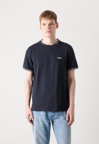 Tamsiai mėlyna medvilninė marškinėliai su trumpomis rankovėmis, su apvalia iškirpte ir baltais dryžiais. "BOSS" logotipas baltos spalvos ant krūtinės.