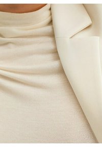 Bluzka w kolorze kości słoniowej o dopasowanym kroju z wysokim dekoltem, wykonana z miękkiej, teksturowanej tkaniny, oraz elegancka biała marynarka z wyciętymi klapami.