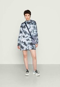 Vestido de manga longa em tie-dye nas tonalidades de cinza e preto, combinado com uma pequena bolsa cinza a tiracolo e ténis preto e branco.