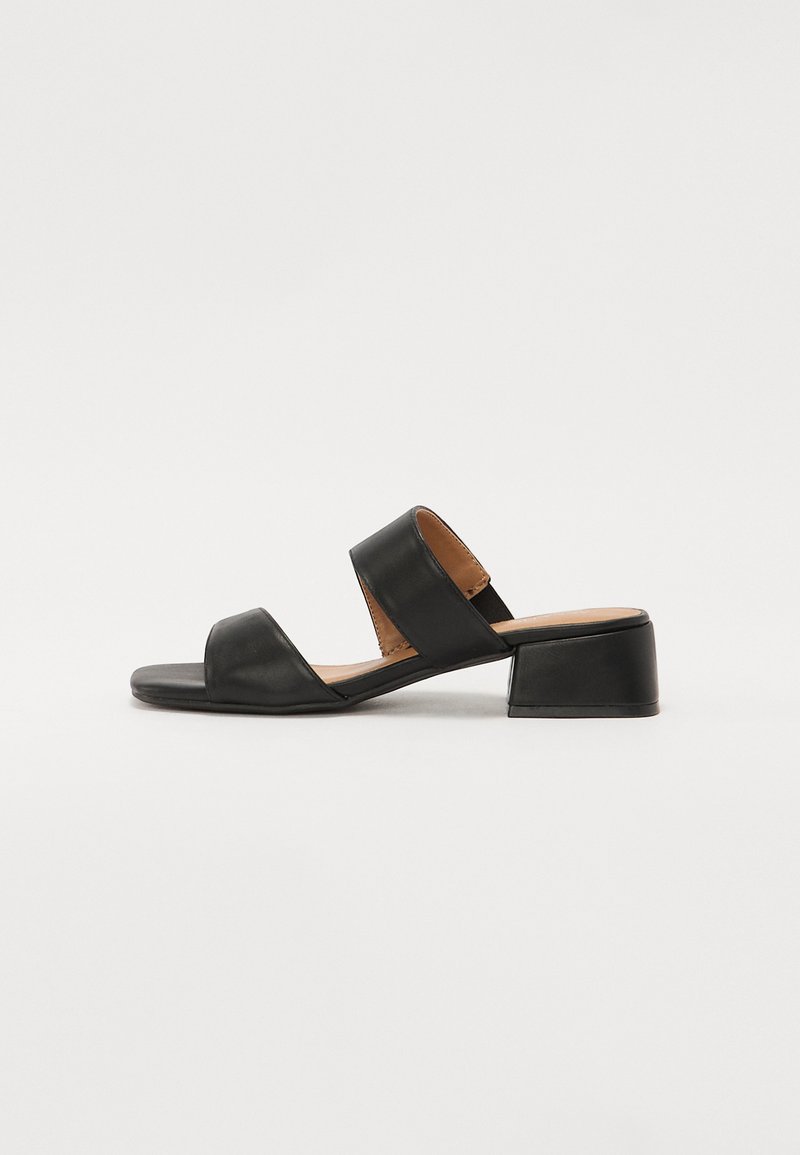 Sandalia de cuero negra con dos correas anchas que cruzan el pie, punta cuadrada y tacón bajo en bloque. Textura suave y diseño minimalista.