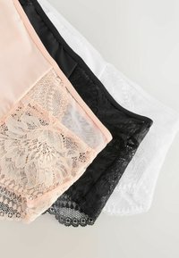 Tre blondebesatte dameundertøj i beige, sort og hvid lagt overlappende på en lys overflade.