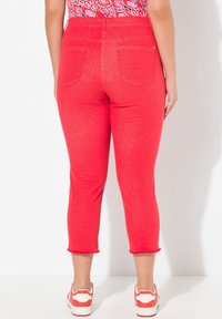 Röda avklippta jeans med fransad nederkant, fem fickor och en åtsittande design. Kombinerat med vita och röda sneakers på en ljus bakgrund.