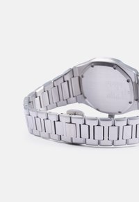 Reloj de acero inoxidable plateado con una caja octagonal sólida. La correa cuenta con eslabones rectangulares y un cierre seguro. La parte trasera tiene un acabado cepillado.