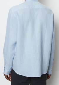 Vaaleansininen pellavapaita, jossa on pitkät hihat, nappikaulus, suora helma ja napitettavat hihansuut. Tekstuuroitu kangas, joka näyttää pehmeältä.