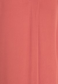 Korallenrote Blusenstoff mit einer weichen, strukturierten Oberfläche. Er zeichnet sich durch ein einfaches Design und einen leichten Glanz aus, mit einer zentralen vertikalen Naht.