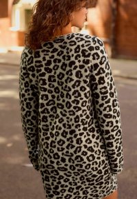 Abito maglione con stampa leopardata, caratterizzato da un knit testurizzato in tonalità di grigio e nero. Maniche lunghe e vestibilità rilassata, che termina sopra la coscia.