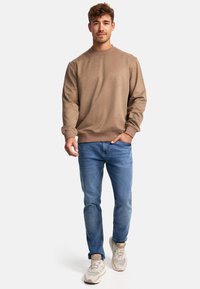 Bruine katoenen sweatshirt met een ronde hals, gecombineerd met blauwe jeans en lichtgekleurde sneakers, met een klassieke pasvorm.