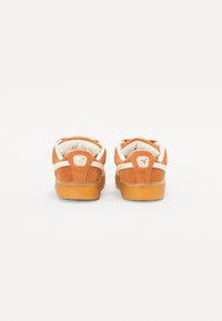 Oransje semsket stoff sneakers med kremfargede detaljer, rund hæl og gummisåle. Har et gullfarget logo på baksiden.