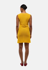 Robe tricotée jaune à design sans manches, présentant un motif texturé, une longueur jusqu'aux genoux et une légère forme évasée.