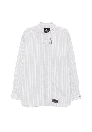 Chemise blanche à manches longues avec fines rayures verticales grises, une petite poche avant et une étiquette noire près de l'ourlet et du col.