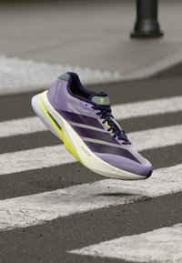 Purple running shoe with a mesh upper. Features white and neon yellow accents, a lightweight sole, and a sleek, aerodynamic shape.