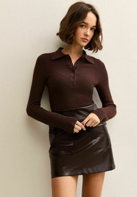 Brązowy prążkowany longsleeve polo z kołnierzykiem i zapięciem na guziki, w połączeniu z czarną mini spódnicą z sztucznej skóry z przednią kieszenią.