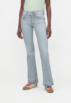 Person trägt hellblaue High-Waist Schlagjeans mit doppelter Knopfleiste und beigen Sneakers mit rosa Schnürsenkeln.