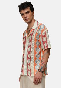 Koszula na krótki rękaw z guziczkami, wykonana z wielokolorowego materiału z mesh teksturą. Posiada mix diamentów oraz falistych pasków w odcieniach pomarańczowego i niebieskiego.