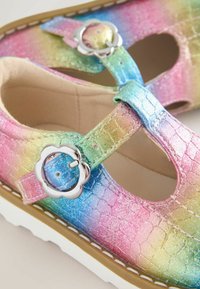 Textured, multicolored, iridescent Mary Jane shoes with a round buckle, showing pink, blue, and green gradient design and cut-out sides.