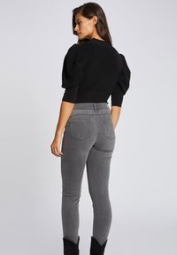 Top nero con maniche a sbuffo e vita aderente, abbinato a jeans grigi a vita alta slim-fit. Tessuto morbido e tasche posteriori discrete. Stivaletti neri.