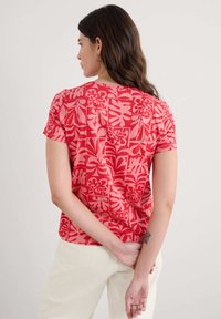 Raudona trumpa rankovė t-shirt turi gėlių raštą skirtingomis rožinėmis atspalviais. Audinys atrodo lygus, su laisvu siluetu.