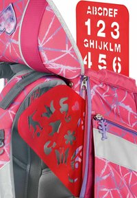Pink backpack with geometric patterns, featuring a textured red stencil pocket and a purple zipper pull, showcasing various cut-out shapes.