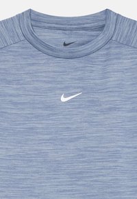 Jasnoniebieska koszulka Nike z okrągłym dekoltem, teksturowanym materiałem z melanżowym wzorem oraz małym białym logo swoosh umieszczonym na środku klatki piersiowej.