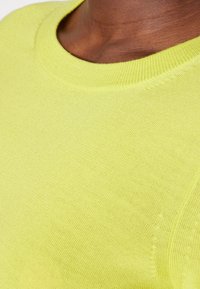 Knit yellow sweater with a round neck, featuring smooth texture and subtle stitching details along the neckline and shoulders.