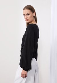 Zwarte lange mouw shirt met gerimpeld detail aan de voorkant, met pofmouwen. Gecombineerd met witte broek voor contrast.