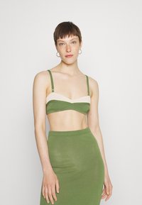 Bralette verde tricotado com uma faixa de cor creme, alças ajustáveis, combinado com uma saia justa verde coordenada. Textura suave, design minimalista.