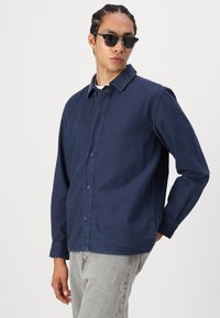 Navy blue button-up shirt made of cotton, featuring a classic collar, long sleeves, and a straight-cut hem, paired with gray jeans.
