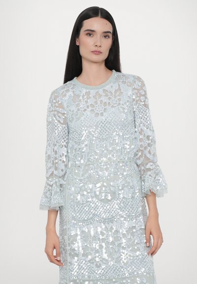 Lyseblå paljetkjole med gennemsigtigt lace overlay, der har flagrende ærmer og intrikate mønstre over stoffet, som skaber teksturerede detaljer.