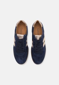 Paire de baskets en daim bleu marine avec des touches beiges et des lacets noirs, vues de dessus sur fond blanc.