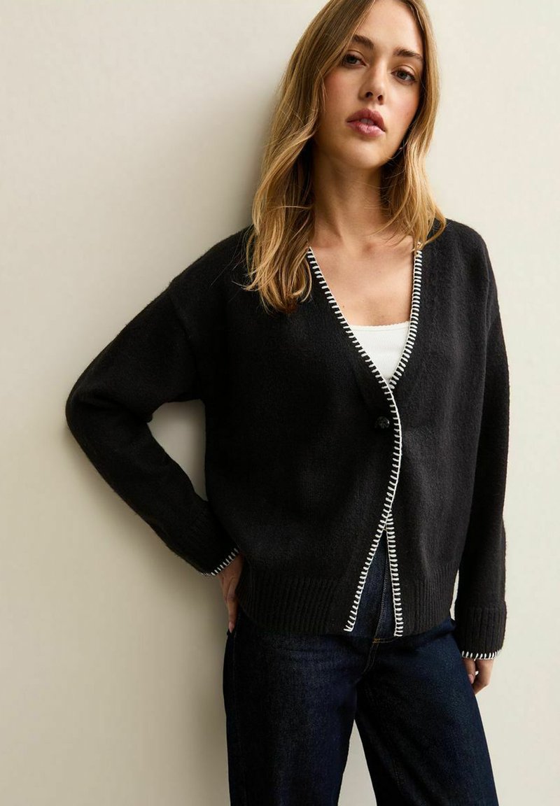 Czarny kardigan z dekoltem w serek, z białym kontrastowym przeszyciem wzdłuż brzegów i mankietów, wykonany z miękkiej dzianiny, z pojedynczym zapięciem na guzik.