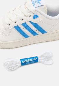 Adidas-sneakers i vitt läder har blåmockastripes, texturerad sula och bomullssnören. Inkluderar ett paket med vita snören med blå branding.