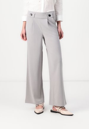 Pantalons larges gris clair avec une texture lisse, dotés d'une taille haute et de deux boutons noirs. Assortis avec des ballerines beiges à lanières.