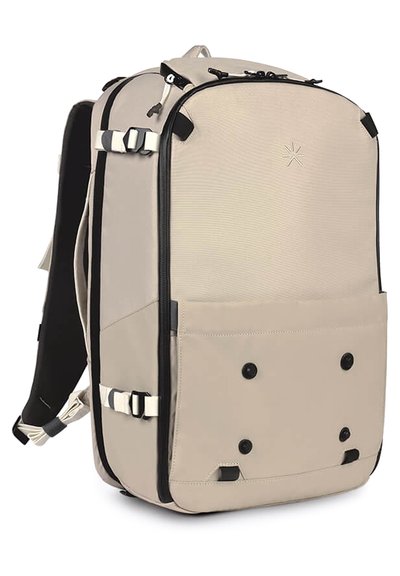 Zaino beige con finitura testurizzata, dotato di un compartimento principale con zip, tasca frontale e spallacci regolabili. Include elementi di hardware neri.