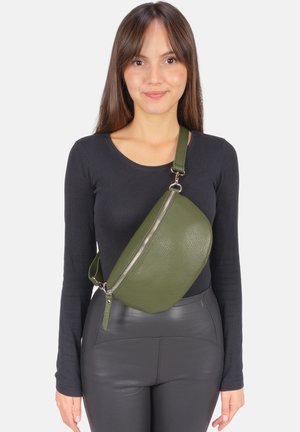 Sac à bandoulière en cuir vert texturé à la forme incurvée, doté d'une fermeture éclair argentée et d'une sangle réglable, porté sur un haut noir.