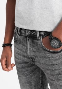 Mustat ja harmaat farkut, joissa on hienovarainen haalistuma, napin suljenta ja etutaskut. Asusteina musta kello ja rannekoru.