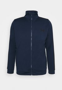 Veste bleu marine avec fermeture éclair intégrale, col haut, manches longues et logo noir discret sur la poitrine gauche.