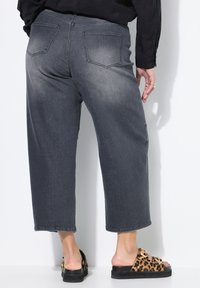 Szare wysokie dżinsy o szerokich nogawkach z delikatnie spranym wykończeniem, dwie tylne kieszenie i surowy dół. W zestawie z czarnymi sandałami w panterkę.