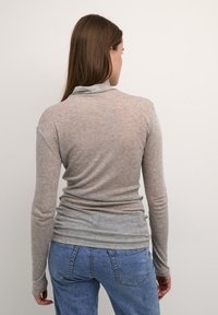 Top grigio a maniche lunghe, tessuto morbido, fabric leggero, colletto arrotondato, dettagli arricciati in vita, abbinato a jeans blu.